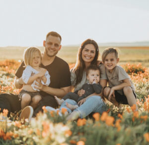 A smiling father, mother and 3 young children are seated in a field of orange flowers.