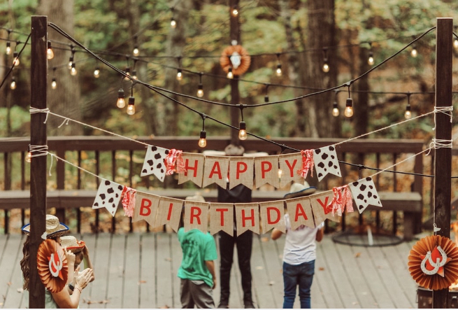 Happy Birthday signs strung across an outside deck with fairy lights and children celebrating.