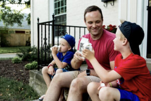father and young children sitting on the front doorstep together and smiling