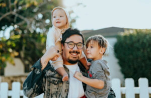 dark haired dad holding his preschooler and toddler in his arms outside