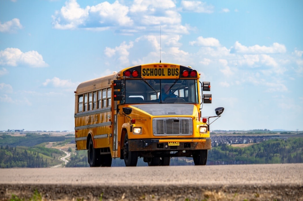 American, yellow school bus driving preschoolers to school under a bright blue sky