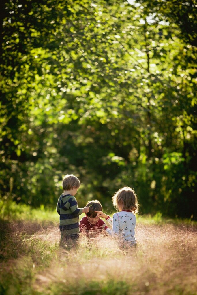 three preschooler children outside under the trees playing together