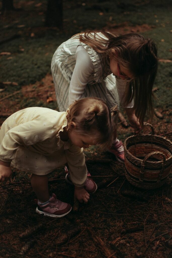 two preschooler girls picking up bits of nature and enjoying tactile experiences outside