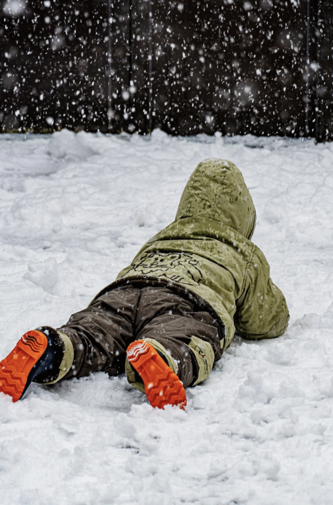 preschooler little boy bundled up in a green hooded coat and red boots for tactile experiences in the snow